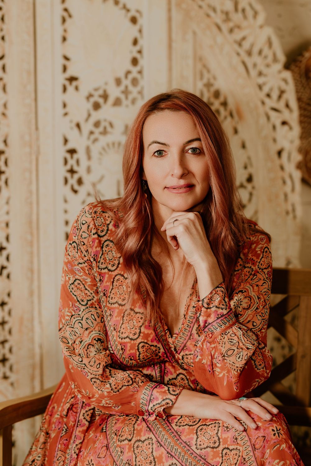 A person in a floral orange dress poses against a decorative white backdrop in a warm-toned photo series.