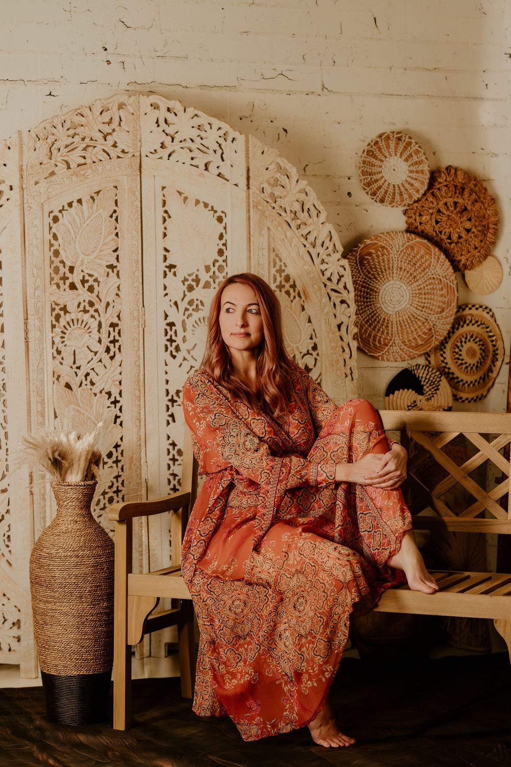 Boho-styled room with decorative screens and woven wall decor features a person in a floral maxi dress lounging.