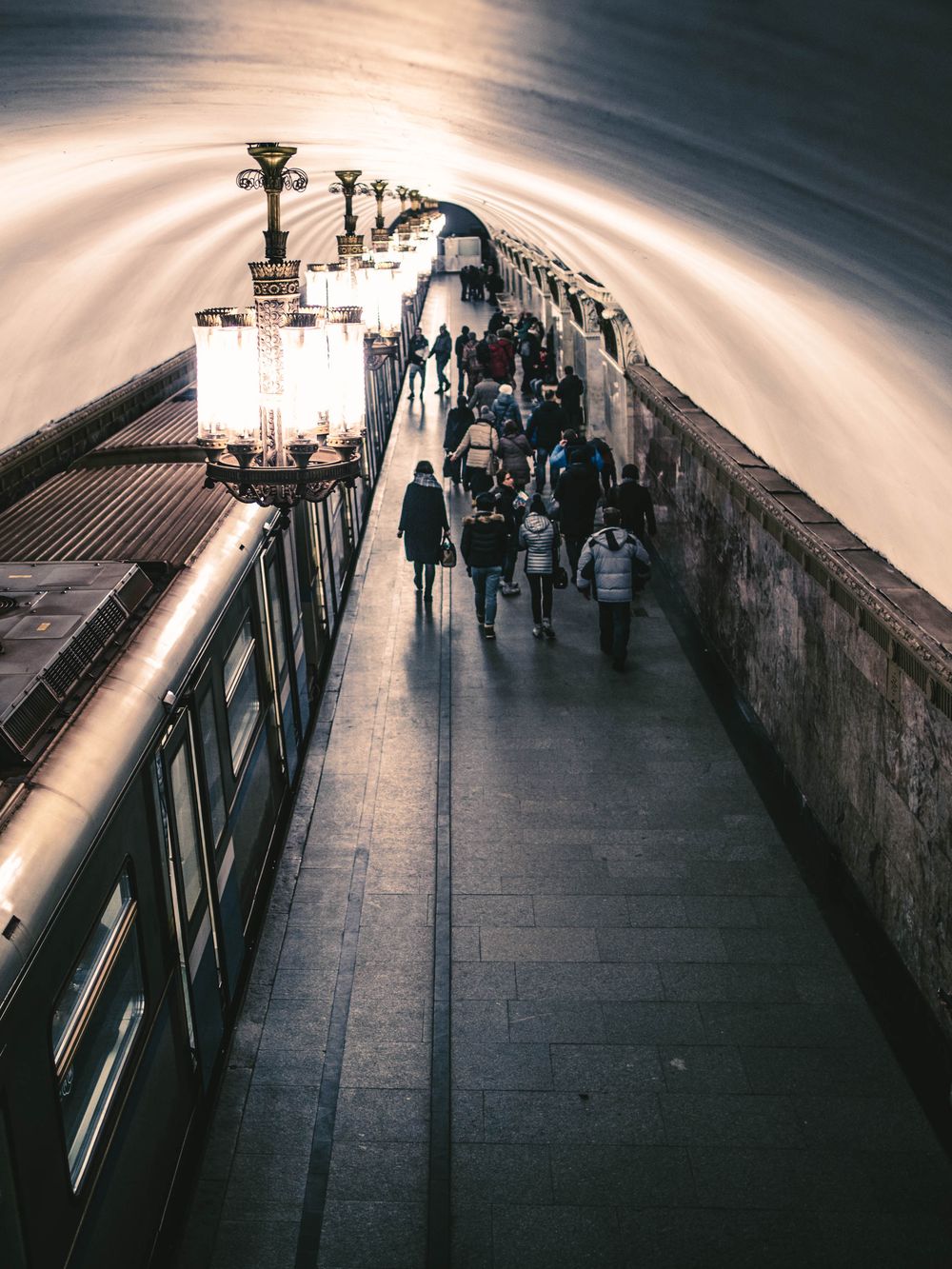 Dramatic perspective shot of a subway platform with commuters silhouetted against bright lighting.