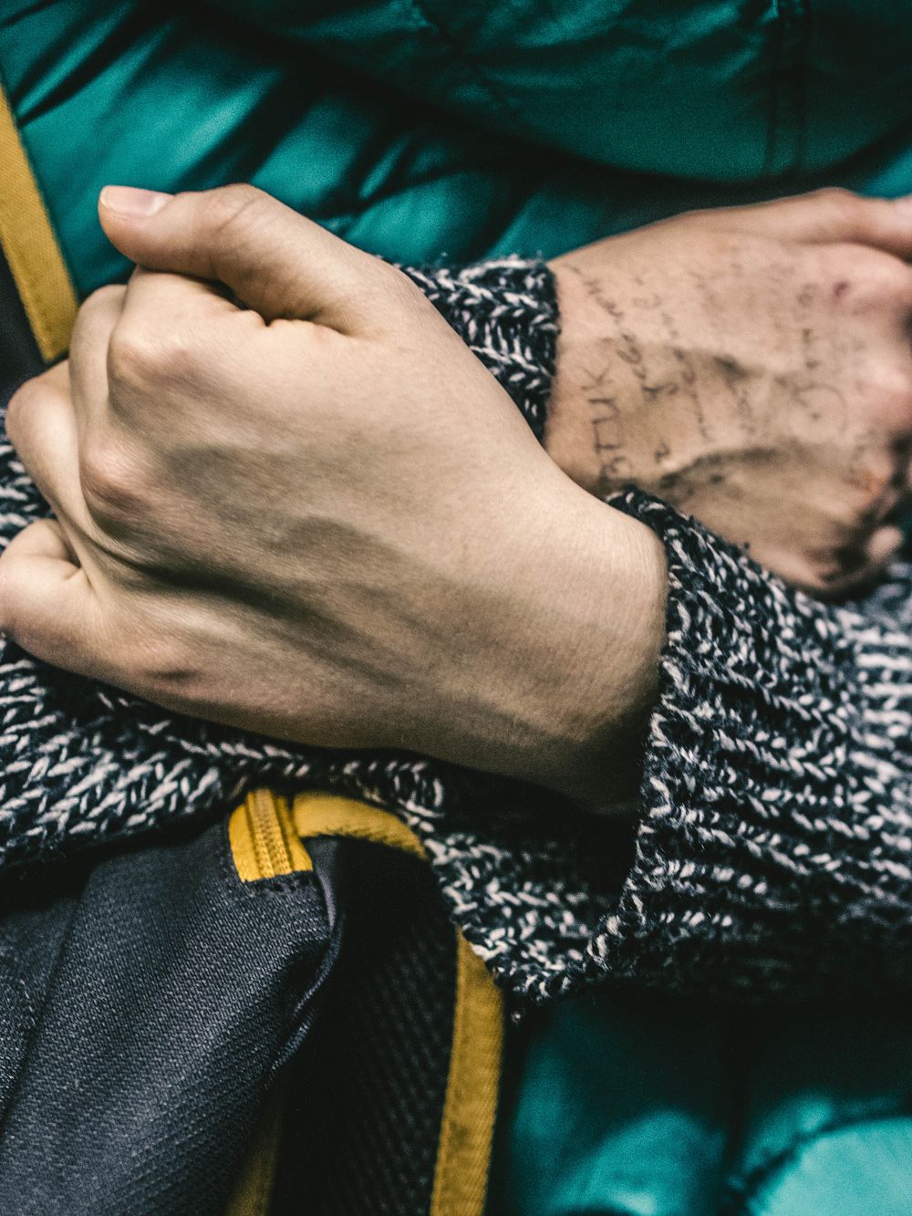 Close-up of hands resting on a cozy knit sweater with black and yellow clothing details in the background.