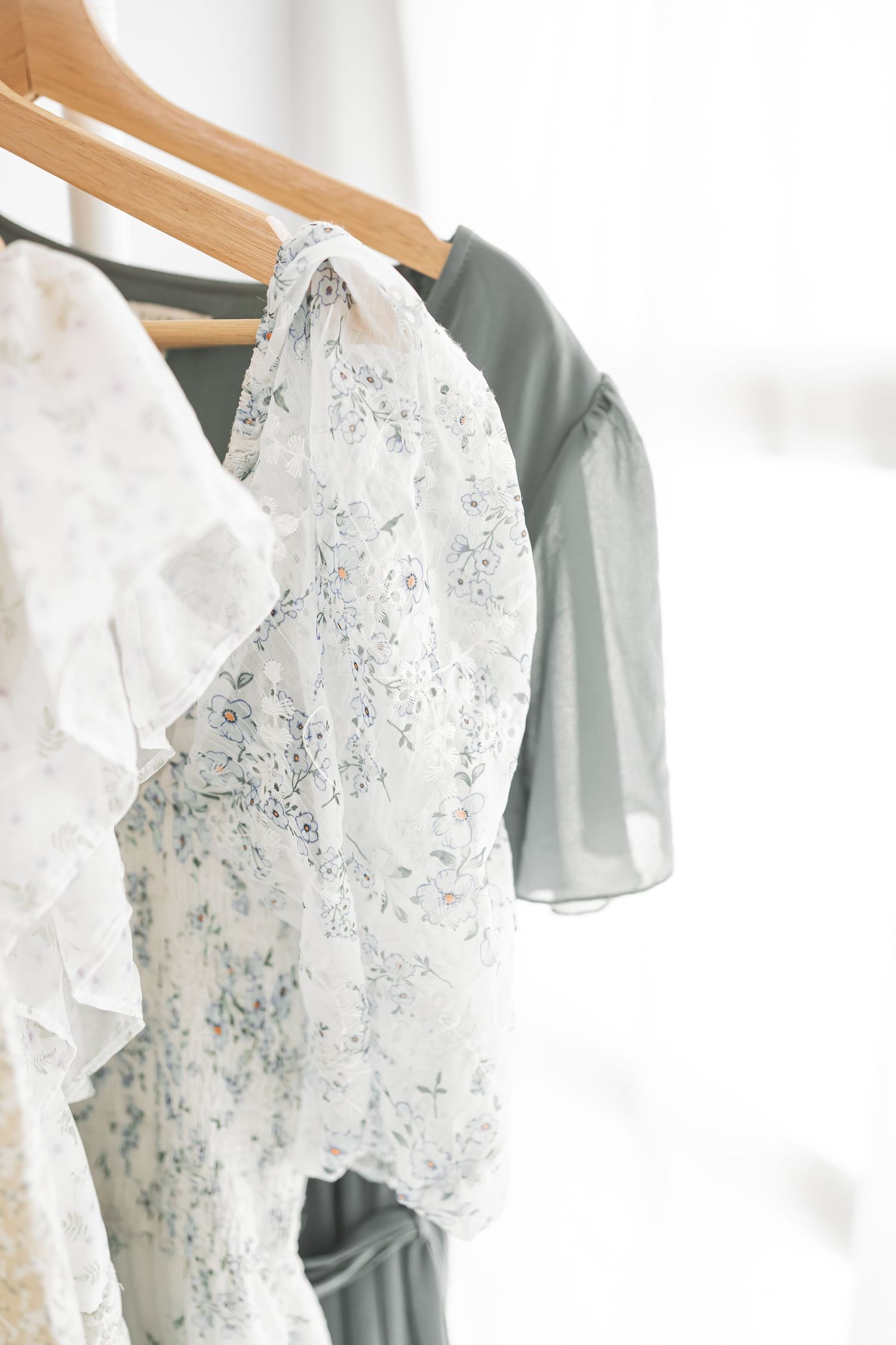 White and gray floral dresses hanging on wooden hangers against a light background.