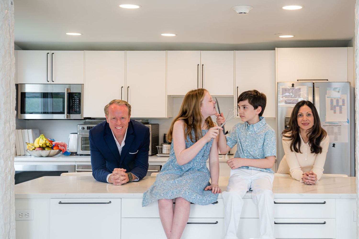 Westport family gather around a modern white kitchen island with the kids making silly gestures while everyone is smiling.