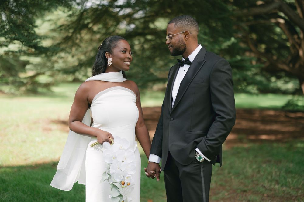 A couple in elegant wedding attire share a tender moment together in a lush garden setting.