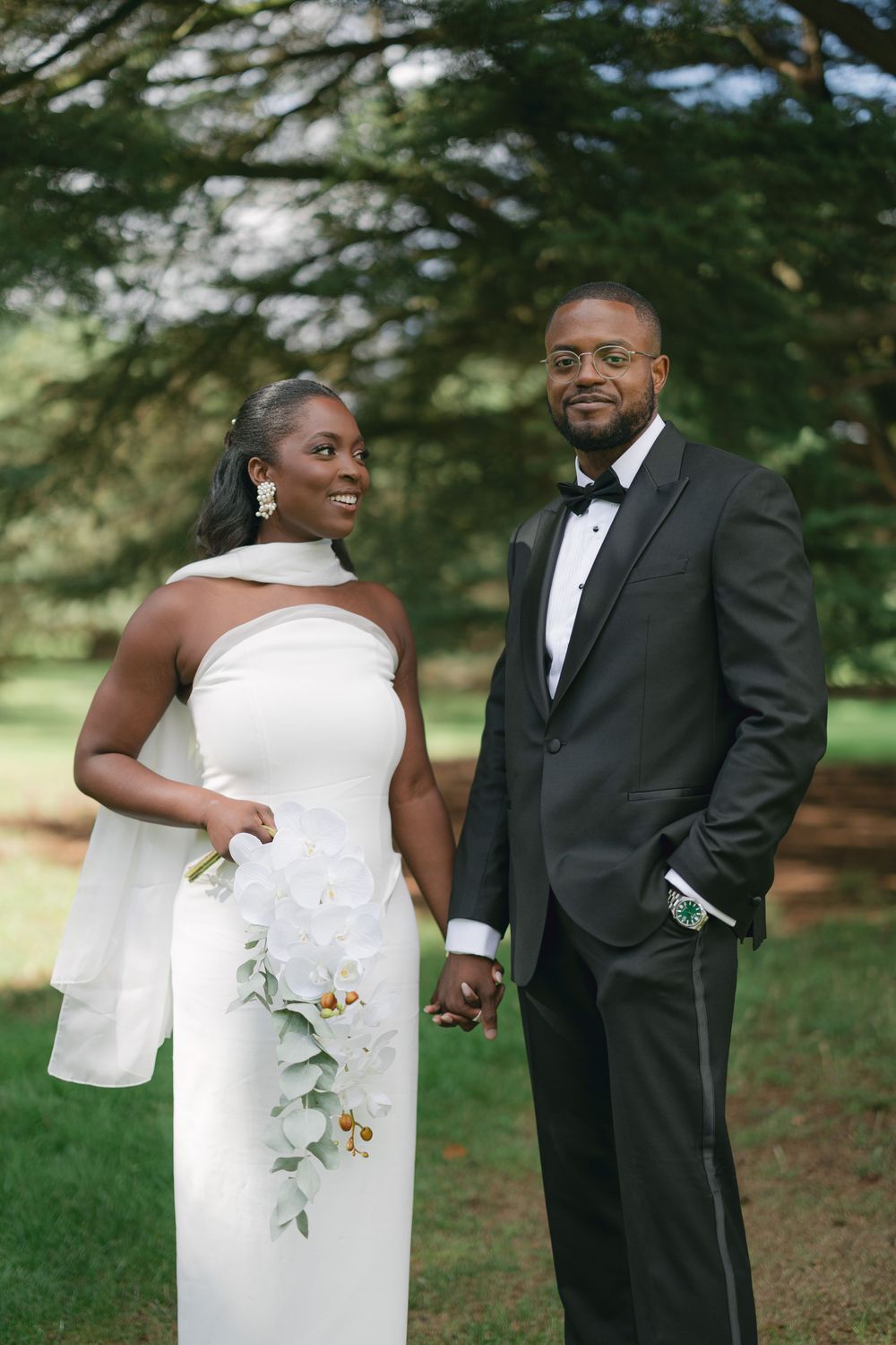 Elegant wedding couple poses outdoors with the bride in a white dress with floral details.