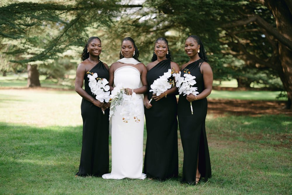 Wedding party members in black and white attire pose together on a green lawn during an outdoor celebration.