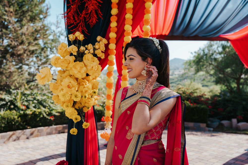 A vibrant red and blue wedding mandap decorated with floral arrangements stands outdoors against a natural backdrop.