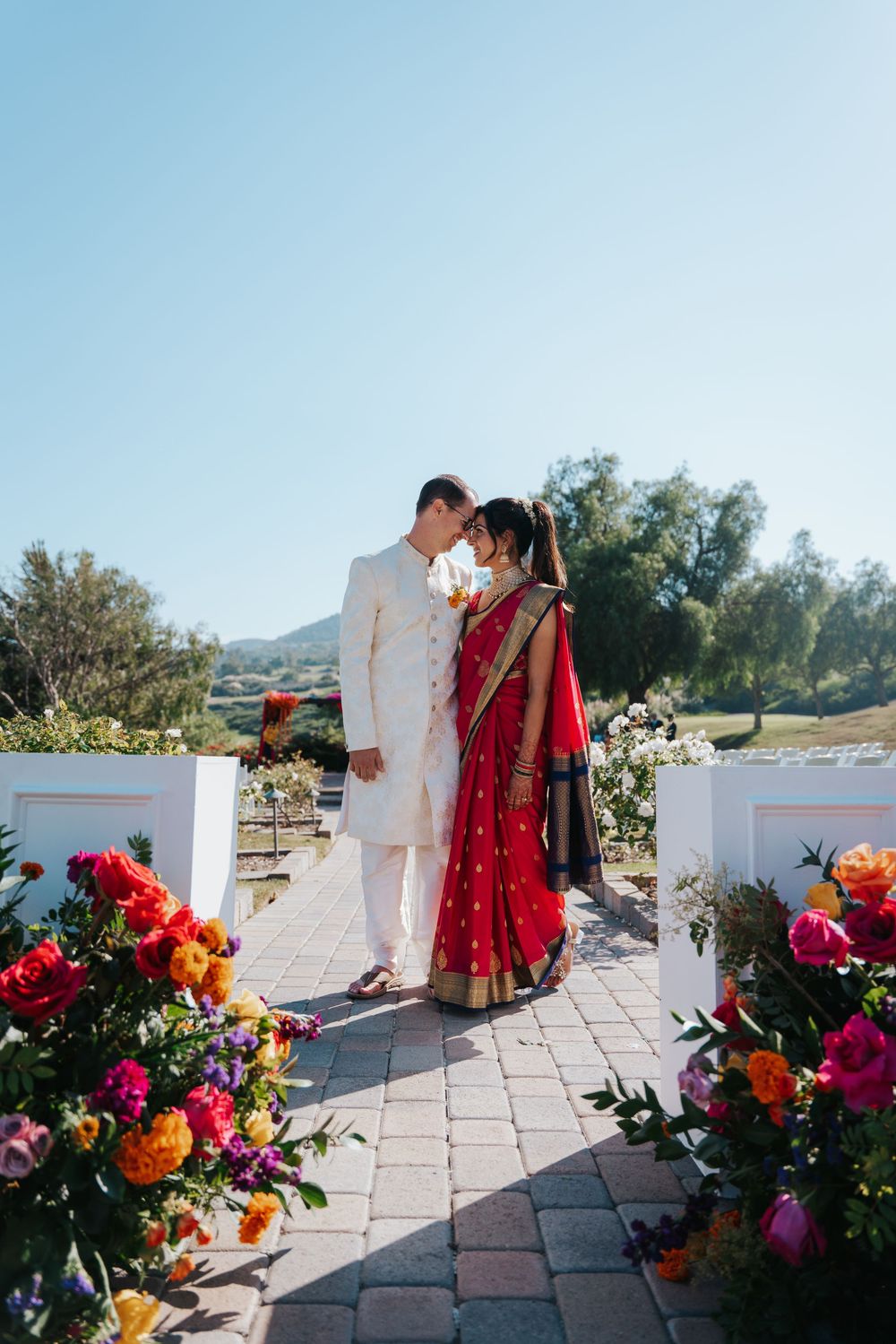 A romantic outdoor wedding scene with colorful floral arrangements and white architectural elements along a stone pathway.