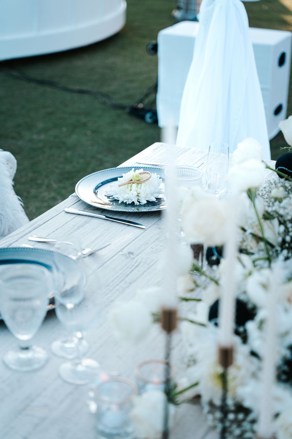White table settings and decorations at an elegant outdoor event with delicate floral arrangements and glassware.
