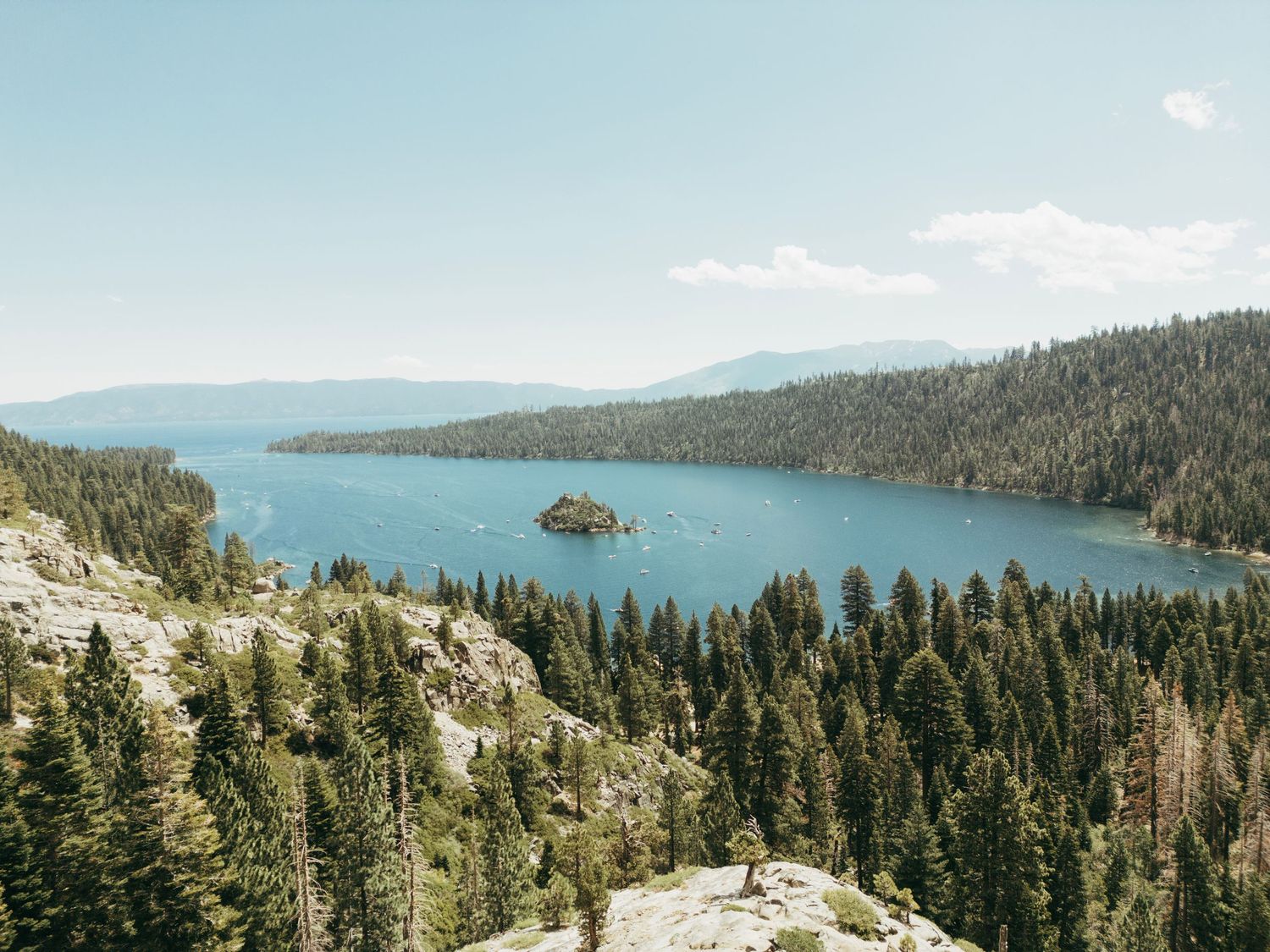 Emerald Bay at Lake Tahoe surrounded by snow-capped mountains and dense pine forests on a clear sunny day.