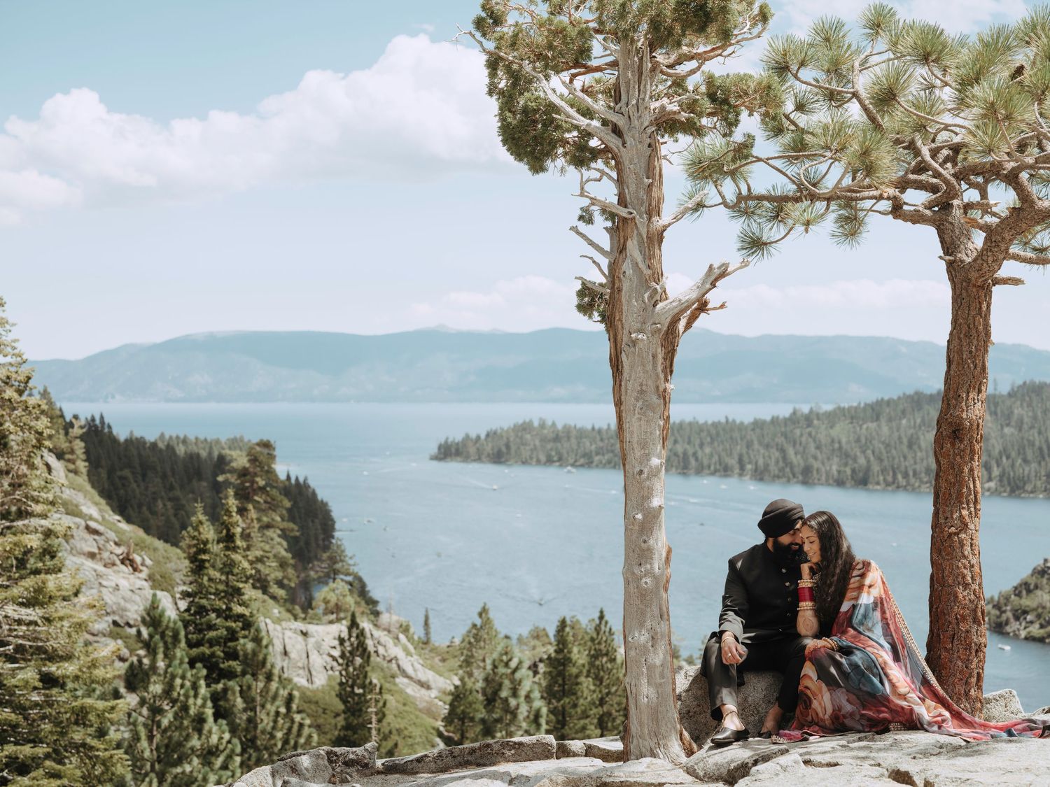 Couple enjoying scenic views from a rocky overlook above a pristine mountain lake surrounded by forest.