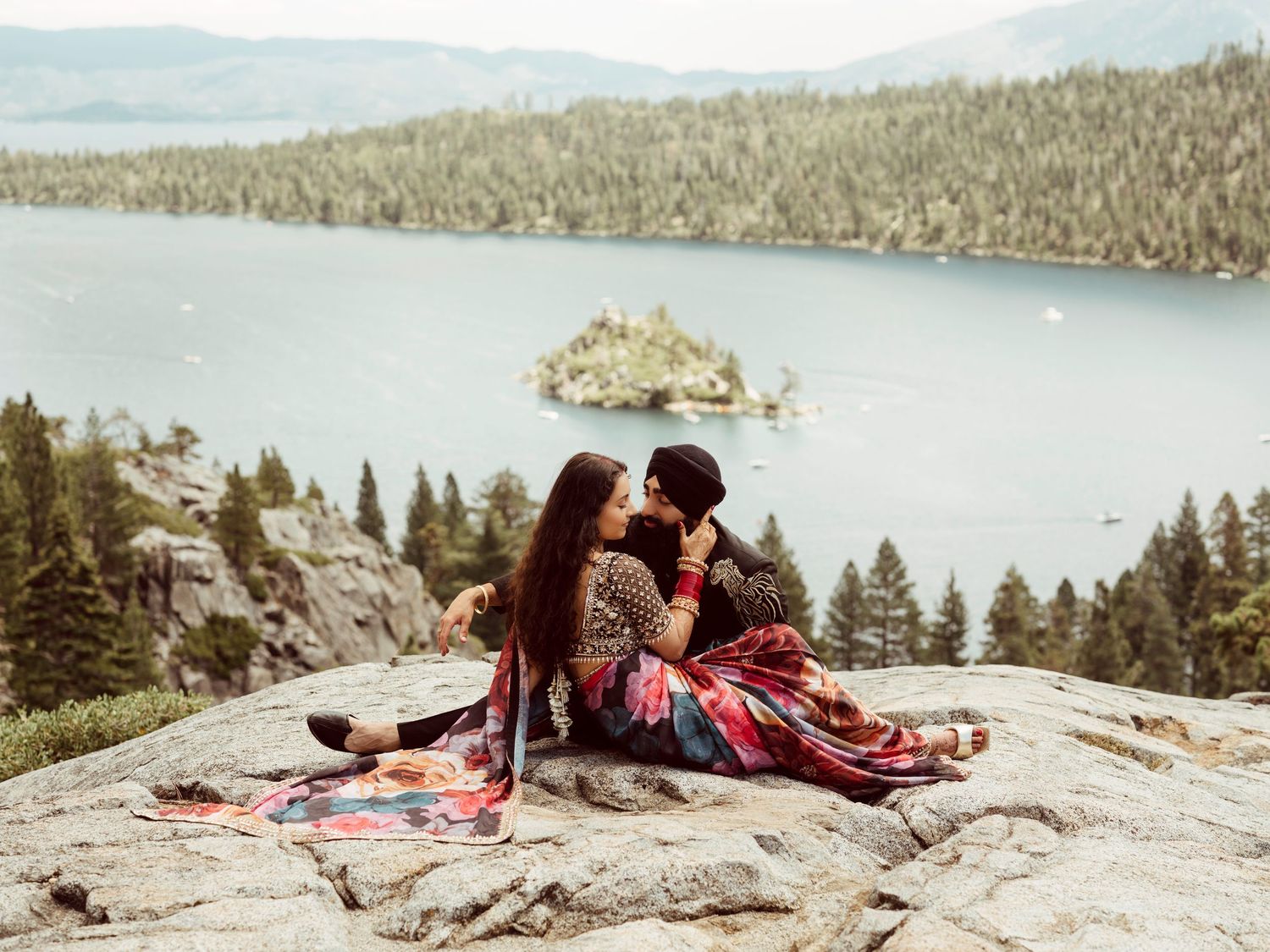 Scenic mountain vista with couple having picnic on rocky outcrop above pristine lake and forest.