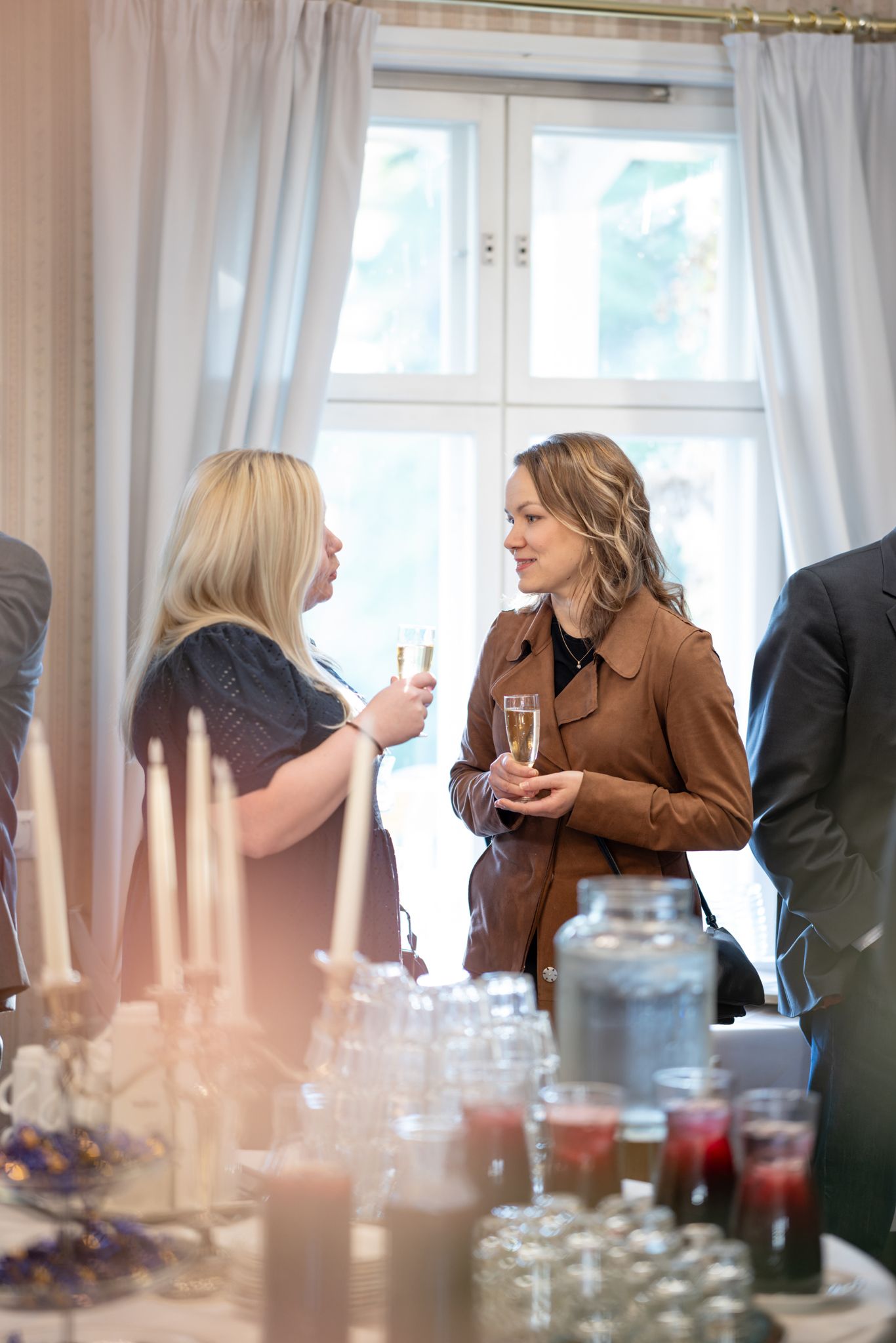People gathered at a table during a social event with glassware and drinks visible in the foreground.