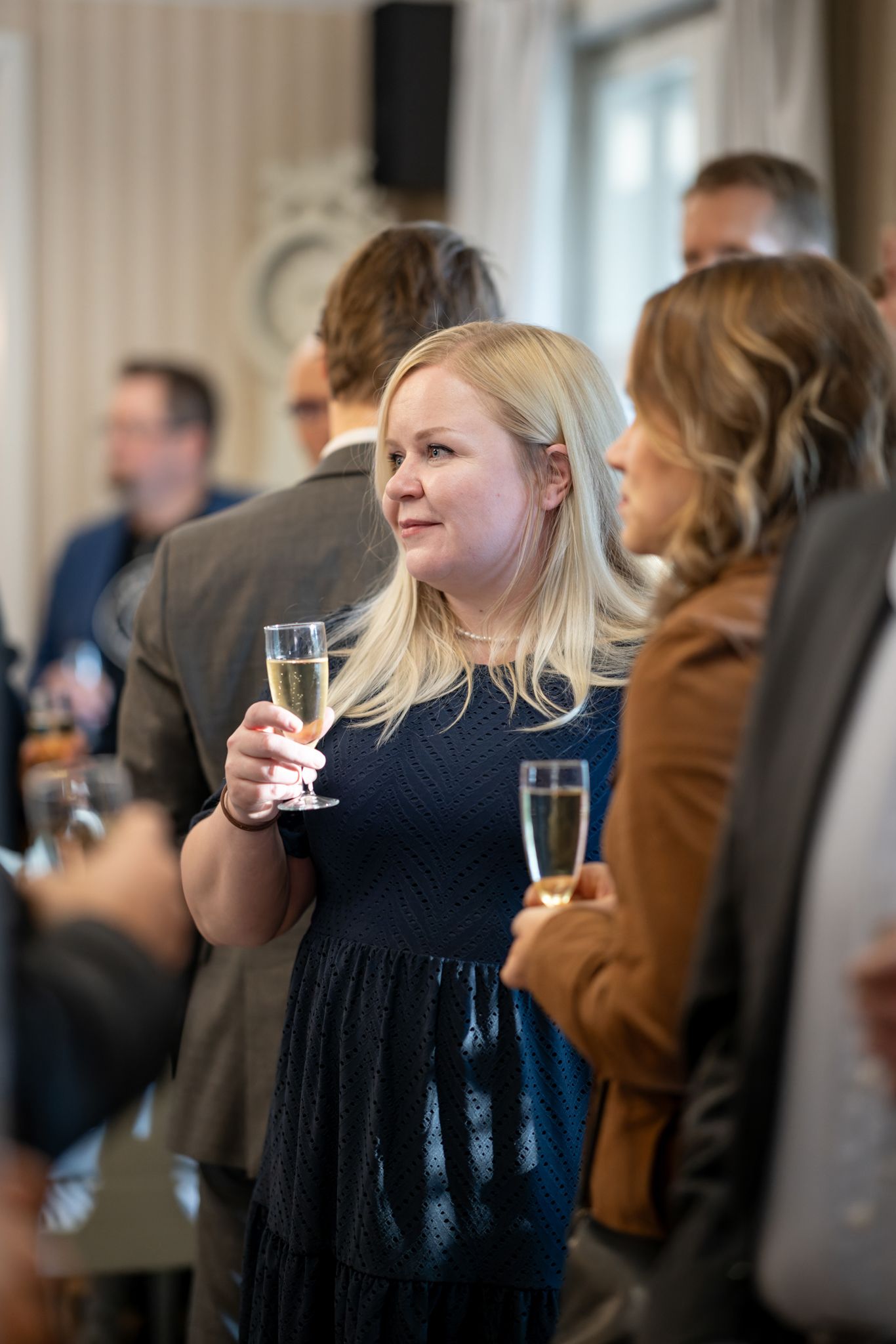 People gather at an elegant social event with champagne glasses, dressed in formal attire for a celebration.
