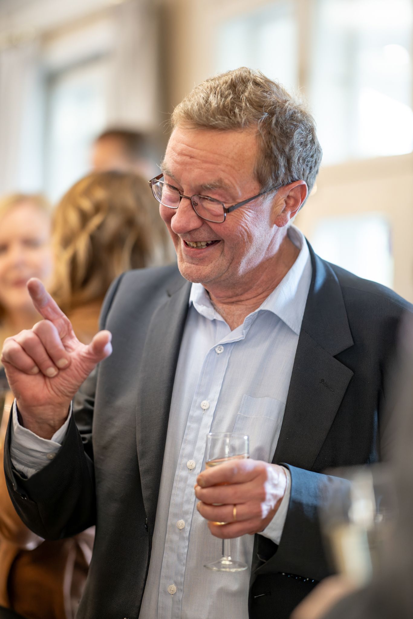 A person in business attire laughs heartily while holding a glass during a social gathering.