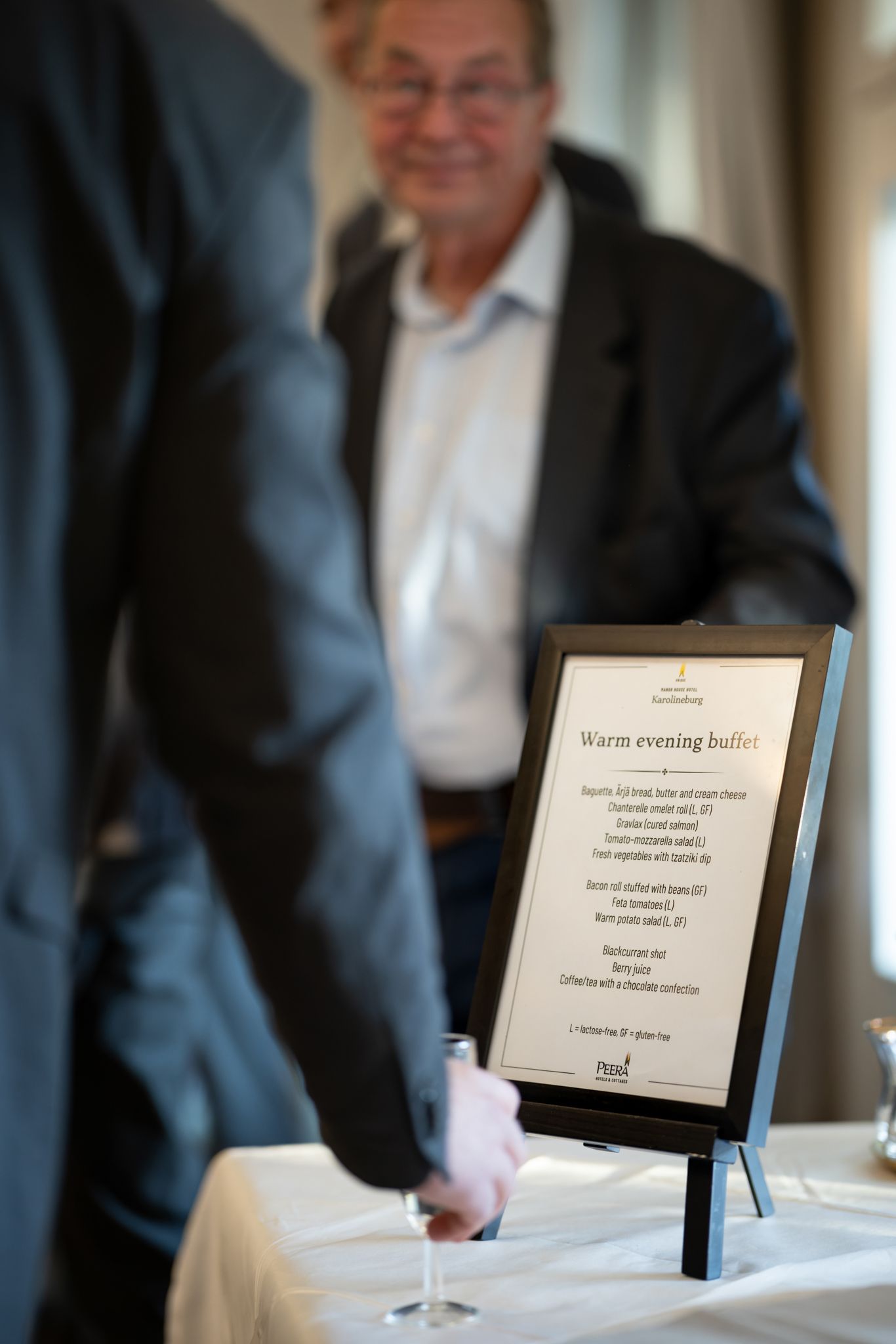 A menu card displayed on a black stand at an elegant dining table with white linens and glassware.