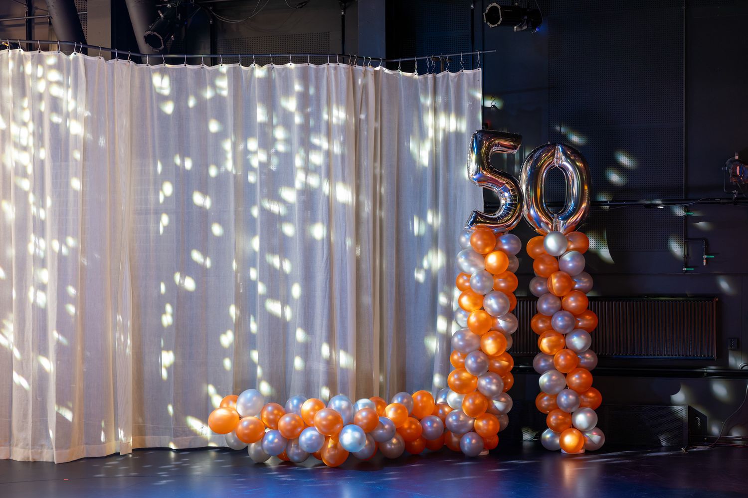 White string lights illuminate a dark room with orange and white balloon decorations creating a festive atmosphere.