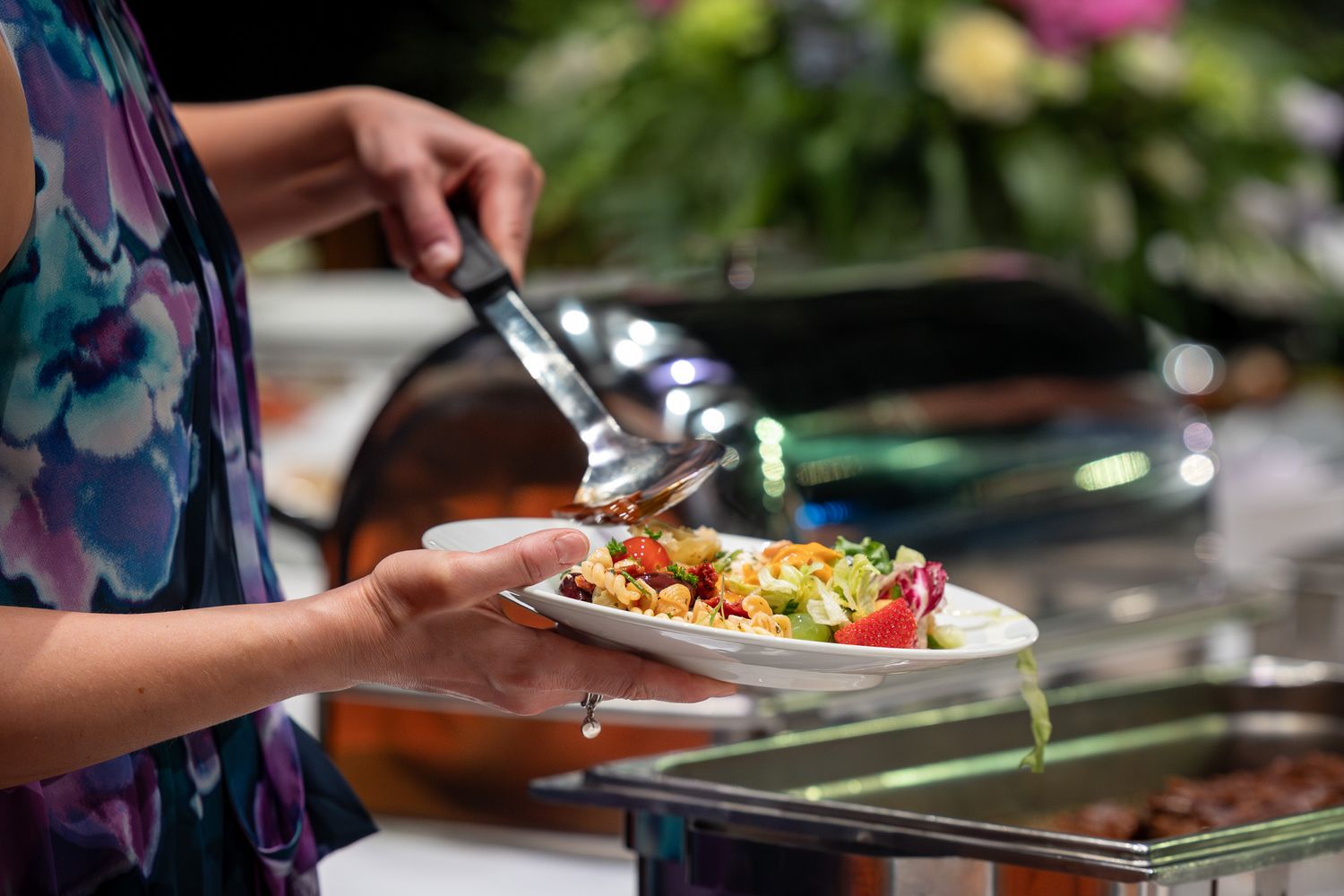 Close-up view of someone serving fresh, colorful Thai food from a buffet line onto white plates.