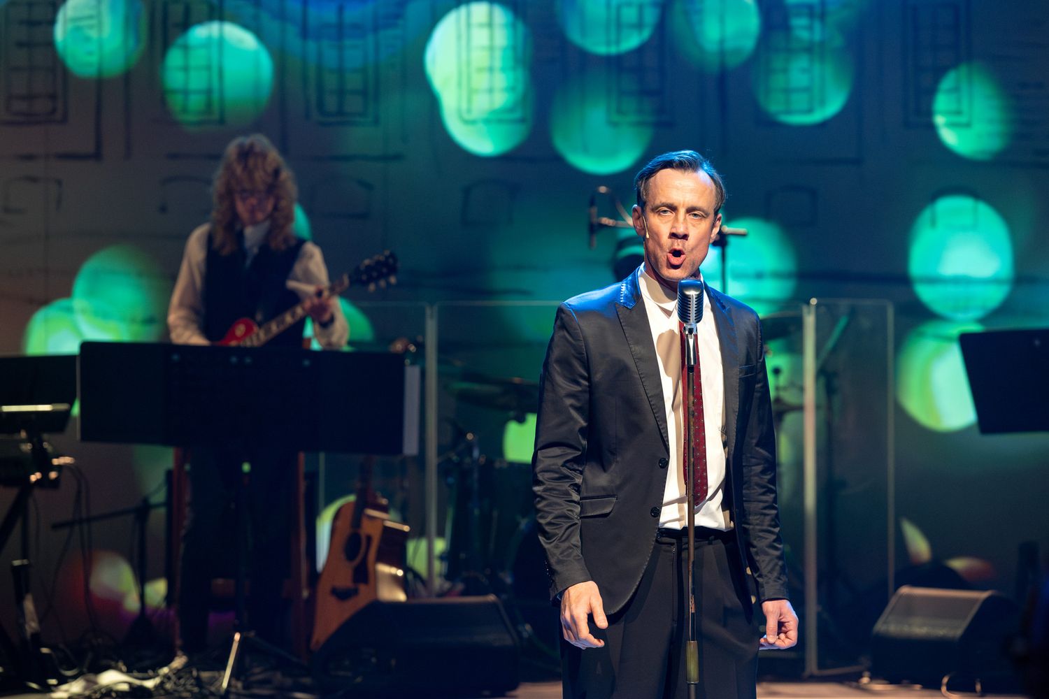 Concert performers on stage with blue and teal bokeh lighting effects in the background.