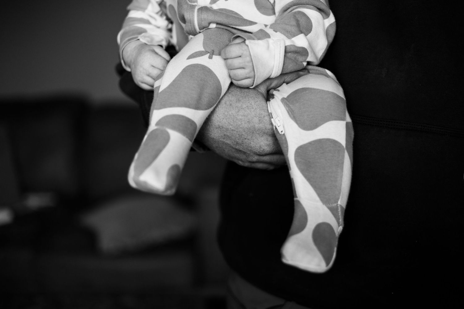 Black and white photo of baby in pear  onesie being held during in-home session | In-Home Family Photos in Westminster, CO