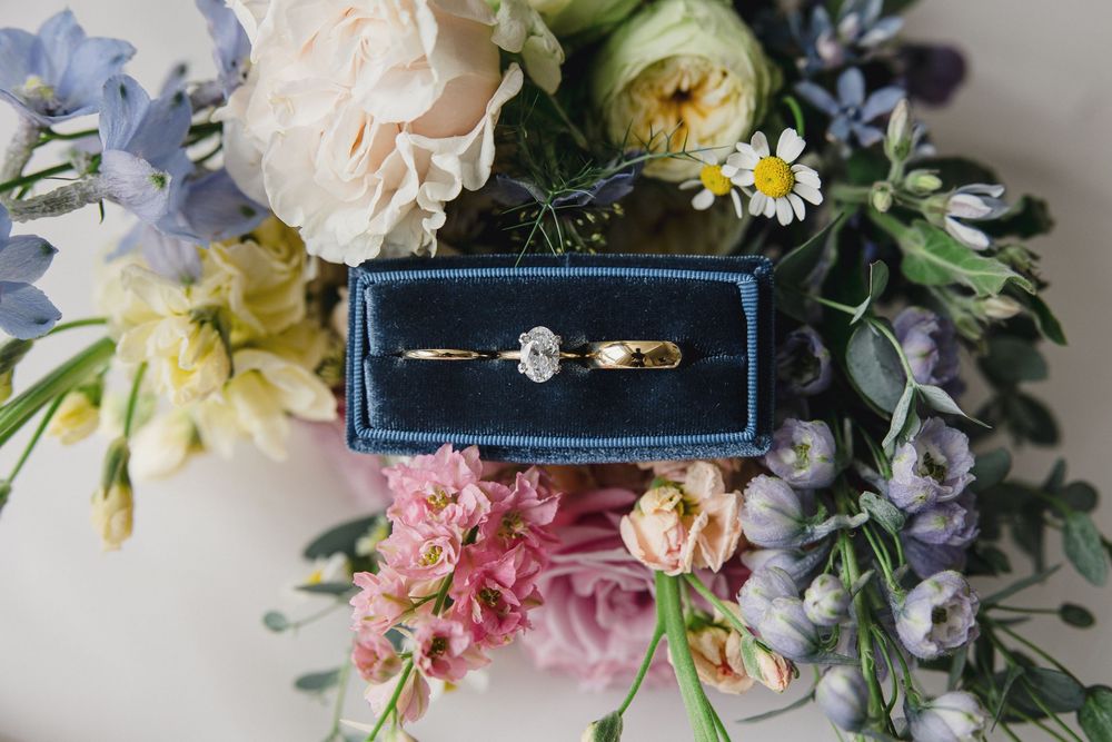 Elegant wedding rings displayed with pastel flowers and greenery on a white surface.