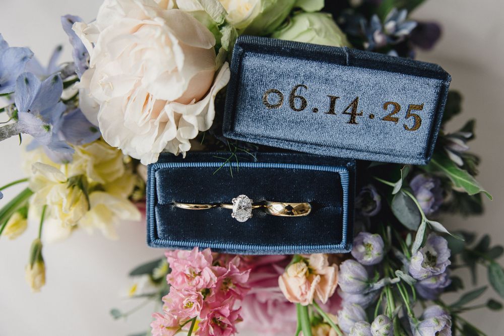 Wedding details including delicate pink and white flowers with a blue velvet ring box displaying elegant engagement rings.