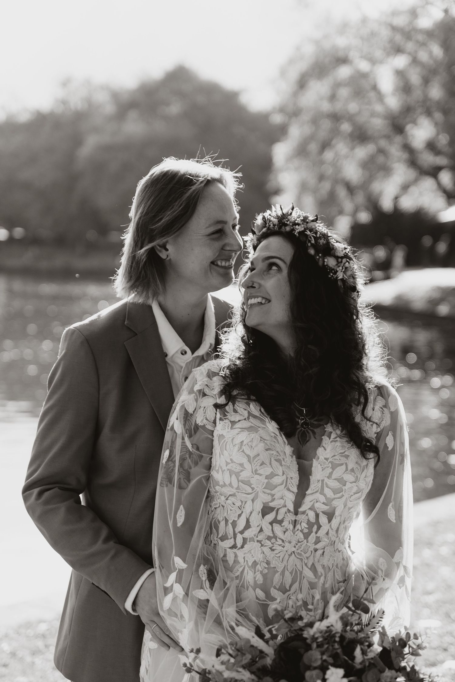 A happy couple shares intimate moments outdoors while wearing a gray suit and white lace dress in a natural setting.