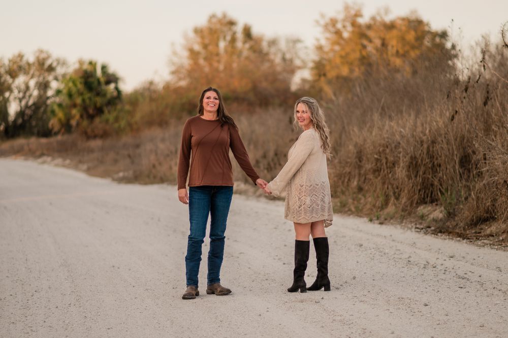 Two people walk hand in hand on a winding dirt path during autumn with golden foliage in the background.