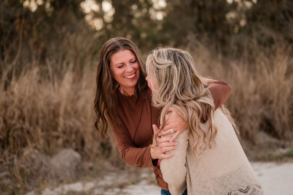 Two people embrace and laugh together on a dirt path during golden hour.