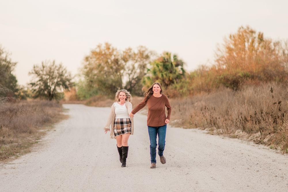 A couple walks together on a winding dirt path with autumn vegetation on both sides.
