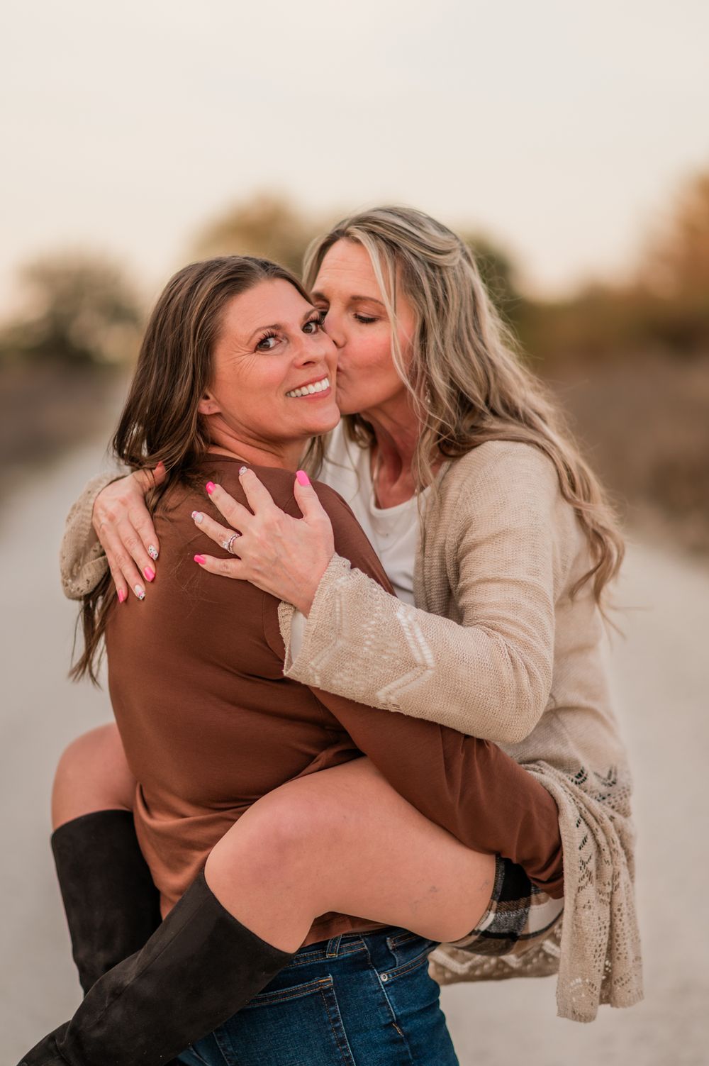 Two people sharing an intimate embrace and kiss outdoors during golden hour while wearing brown and beige sweaters.