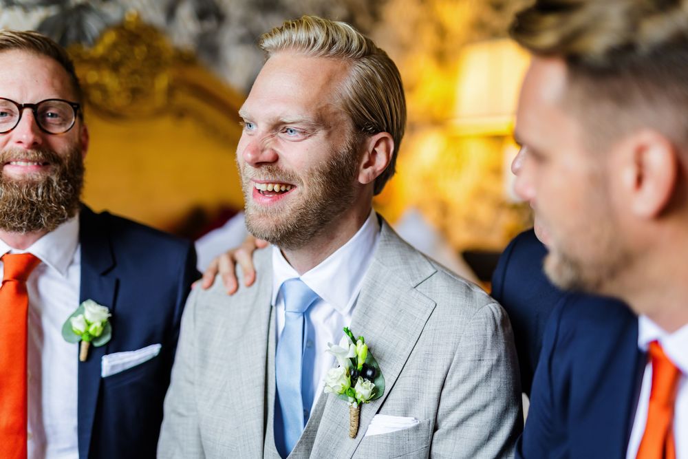 Groomsmen in navy and gray suits with white boutonnieres share a candid moment at a wedding celebration.