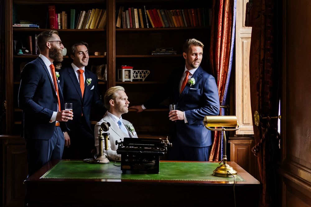 People in formal business attire engage in conversation while standing near a bookshelf in an elegant office setting.
