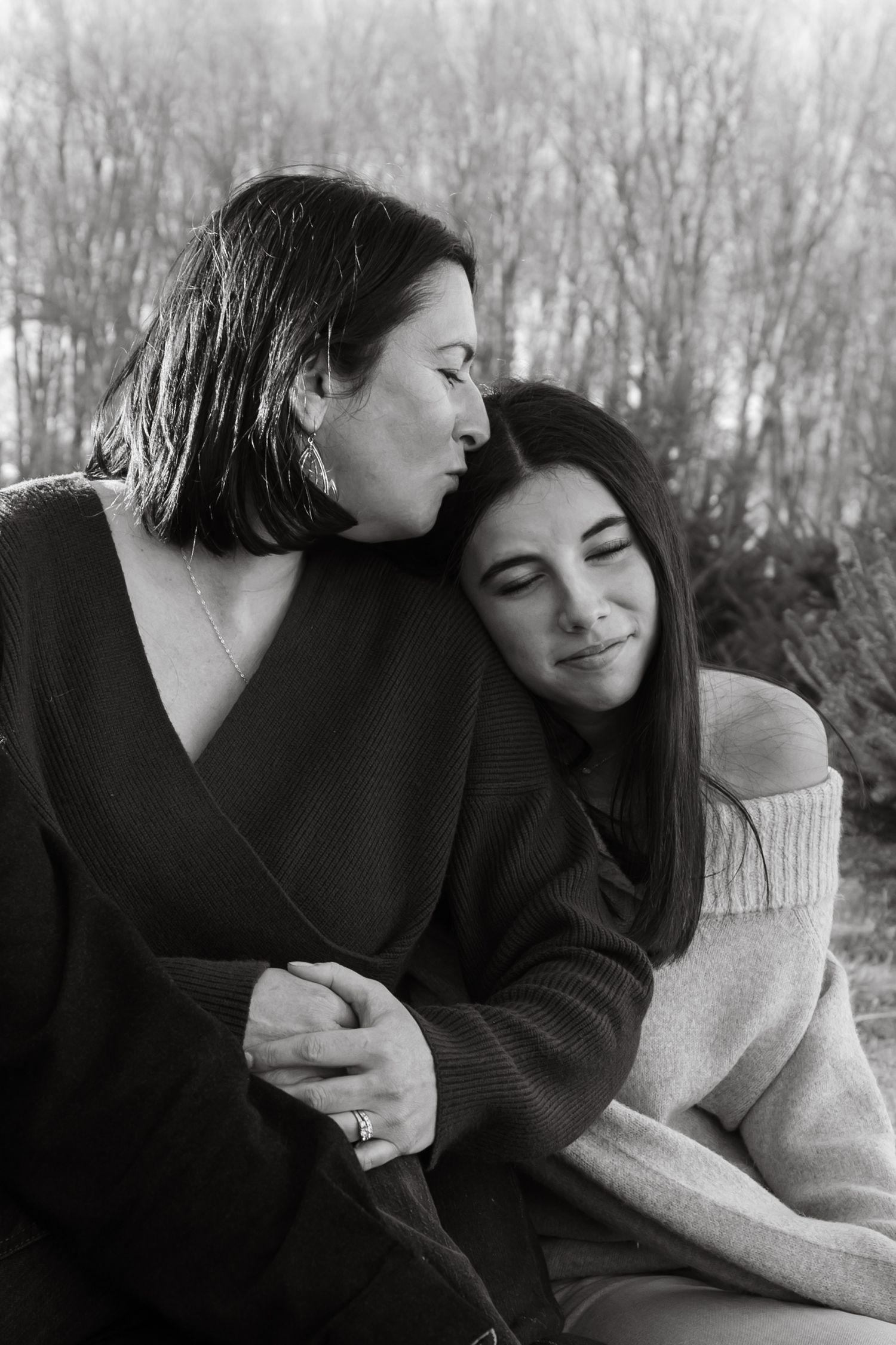 A tender black and white photo series showing a mother and teenage daughter in warm sweaters sharing intimate embraces in nature.