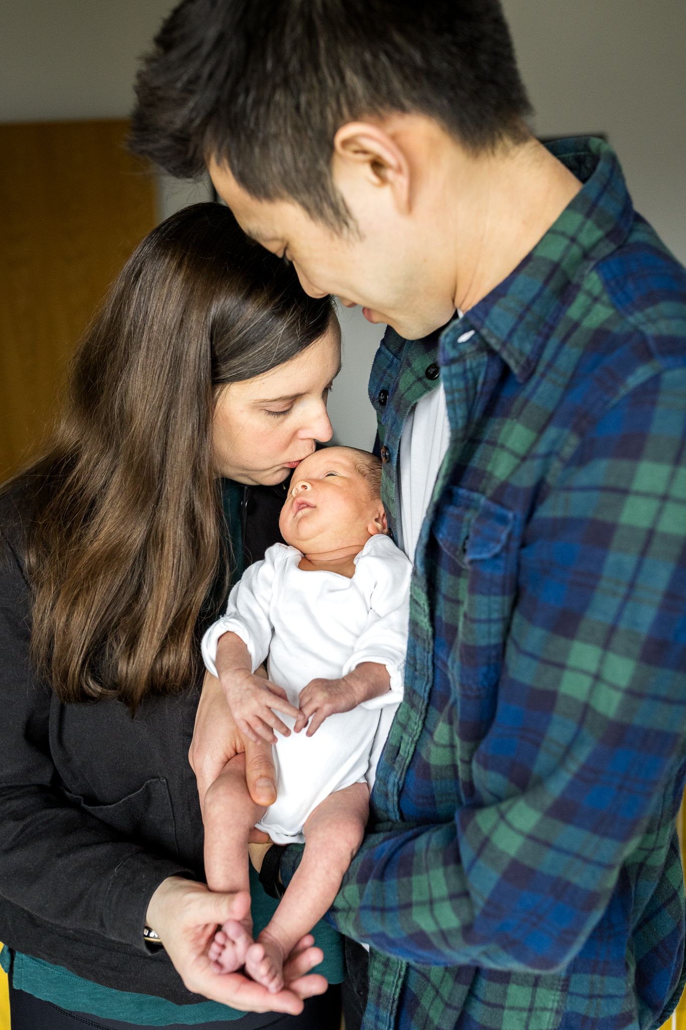 mum kissing her newborn baby girl on the forehead whilst dad looks on