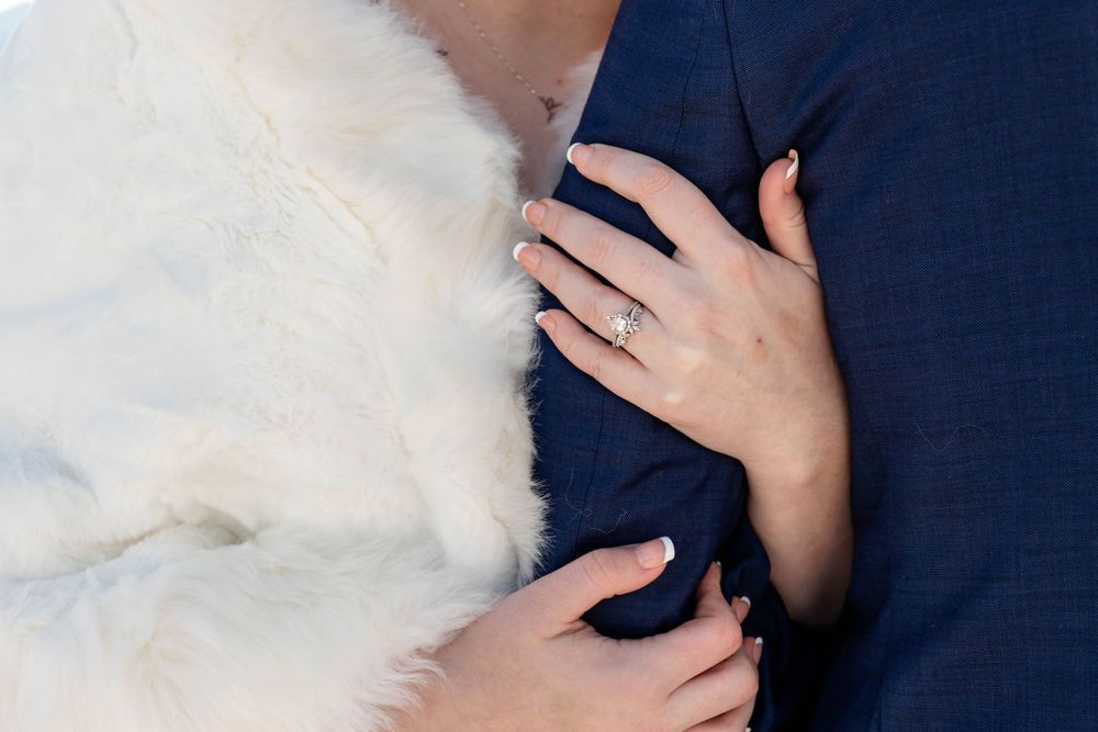 Close-up shot of hands wearing elegant rings against a navy blue suit and white fur.