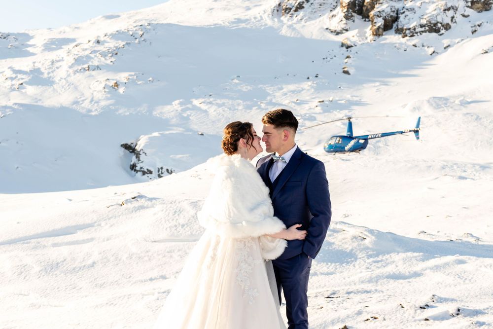 A romantic winter wedding moment captured against a snowy mountain backdrop with a helicopter.