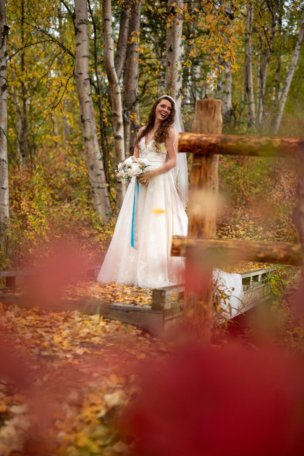 A bride in a flowing white dress poses among autumn birch trees with golden leaves.