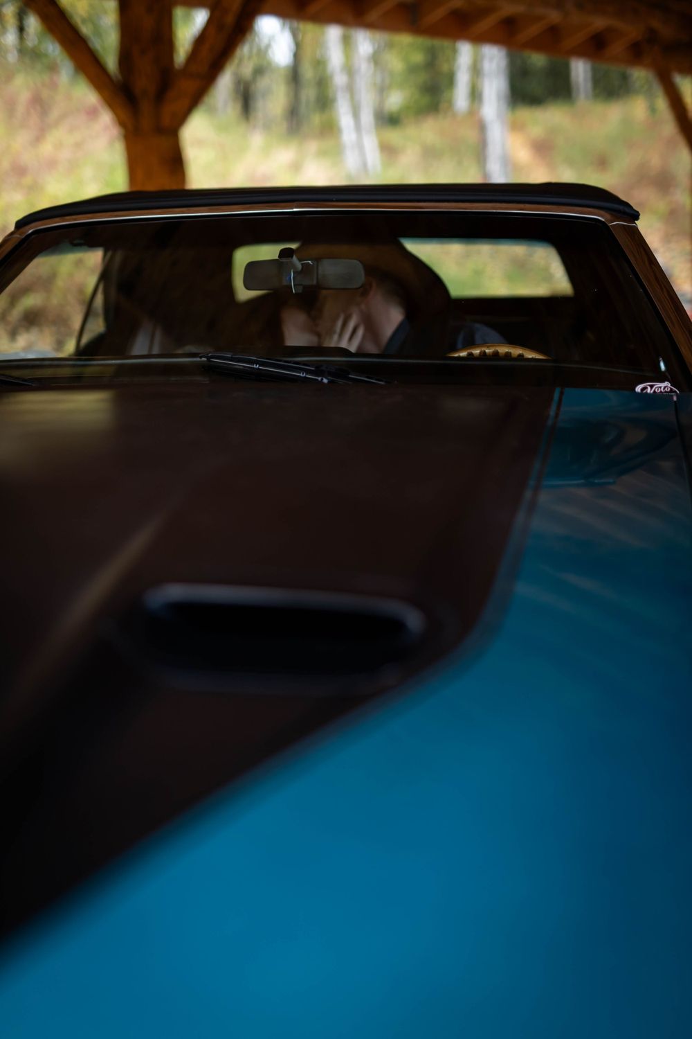 Abstract view of a blue classic car hood and windshield under a wooden shelter.