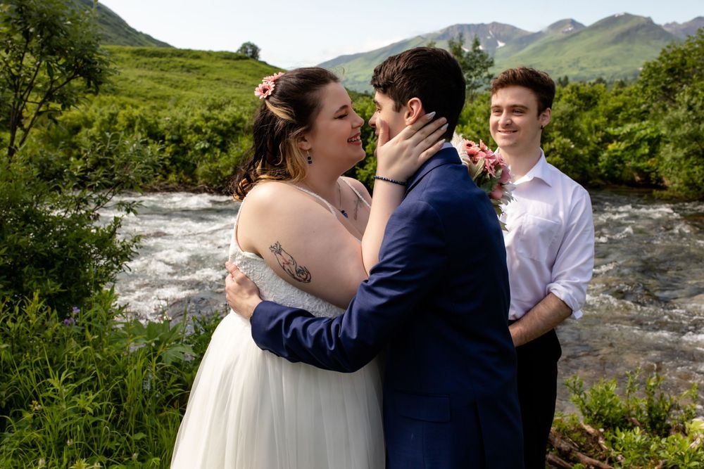An intimate wedding ceremony beside a rushing mountain stream with green hills in the background.