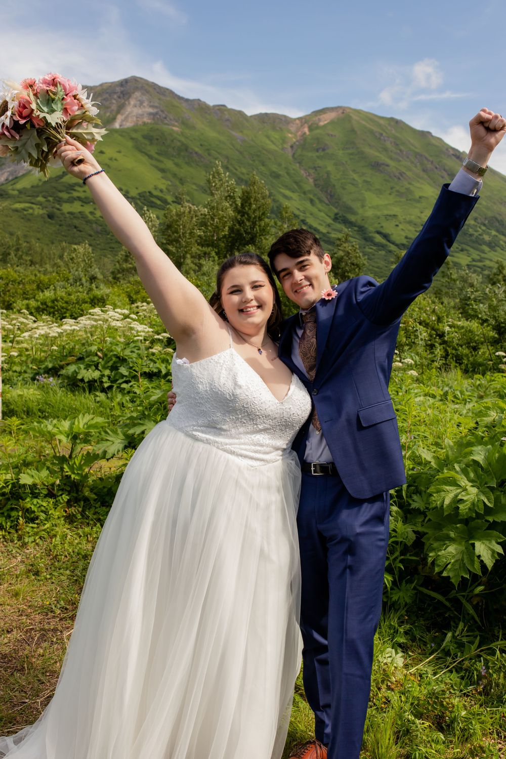 Joyful newlyweds celebrating with raised arms against a backdrop of lush green mountains.