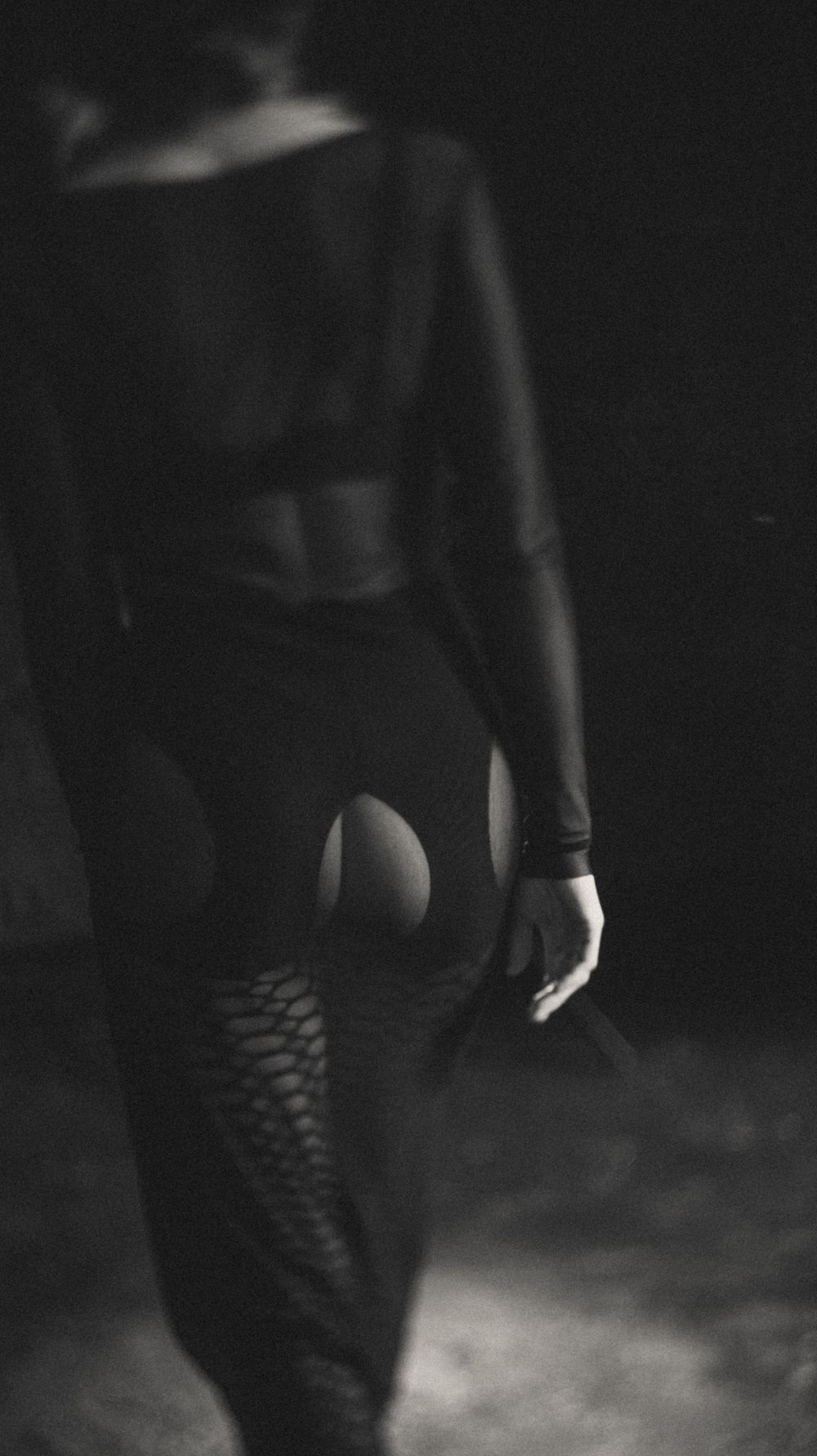 Silhouette of legs in fishnet stockings against dark moody background.