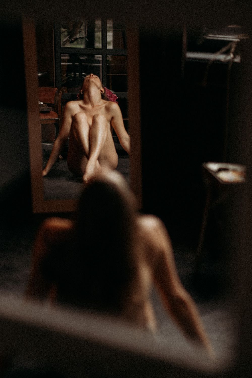 An artistic boudoir photo showing a reflection in a mirror in a dimly lit room with moody lighting.
