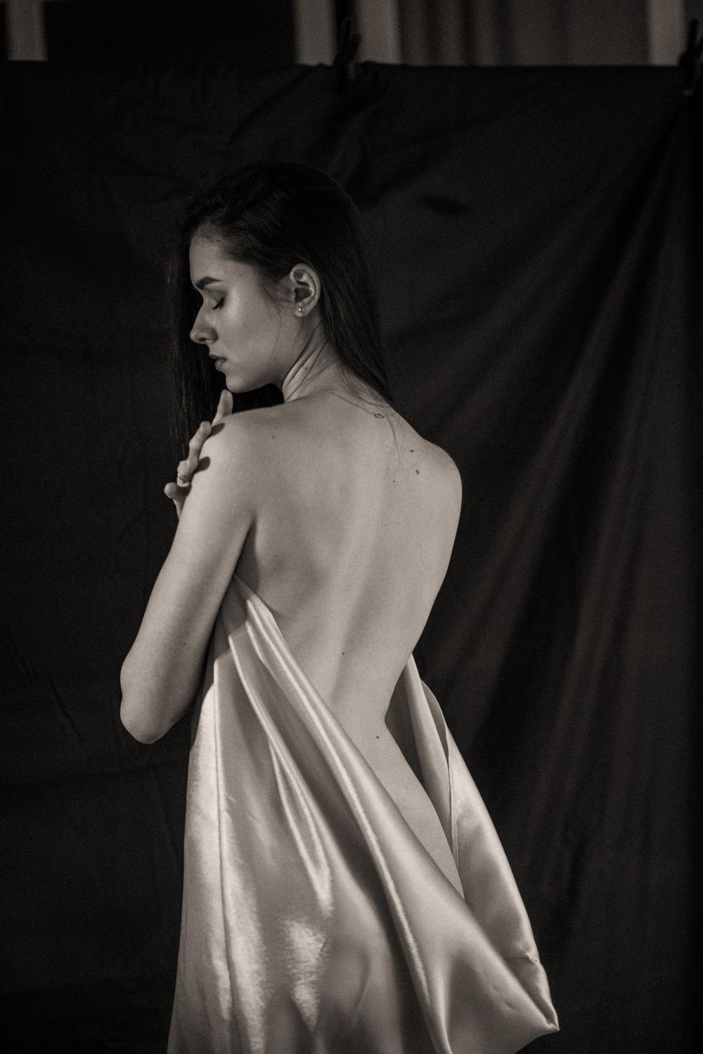 Dramatic black and white artistic portrait series showing a figure's bare back against dark fabric backdrop.