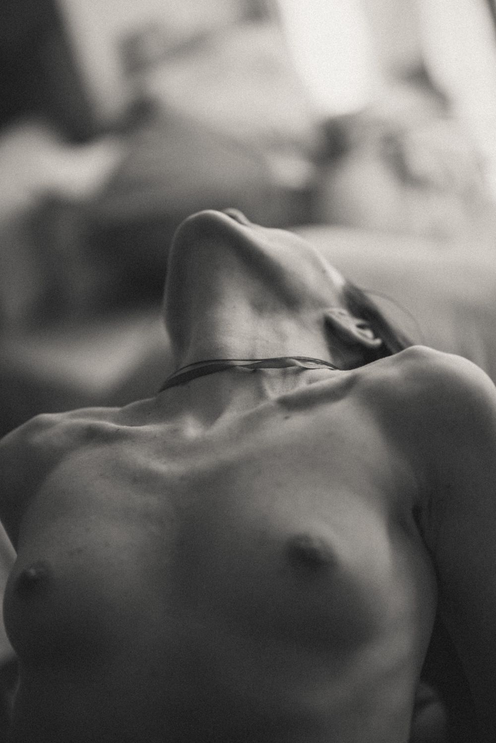 A black and white artistic photograph shows a reclining figure in soft focus with dramatic shadows and highlights.