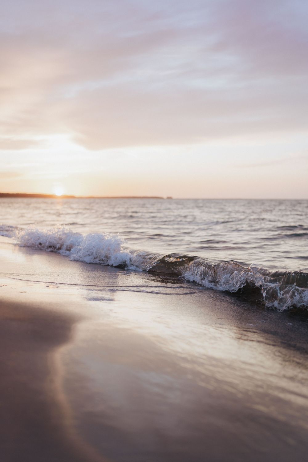 Gentle wave crashes on beach at sunset creating magical golden reflections on wet sand.
