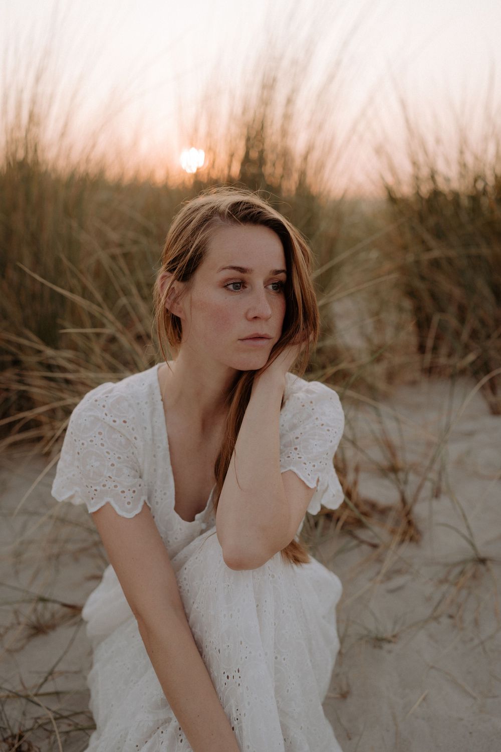 Dreamy beach portrait in white eyelet dress during golden hour sunset.