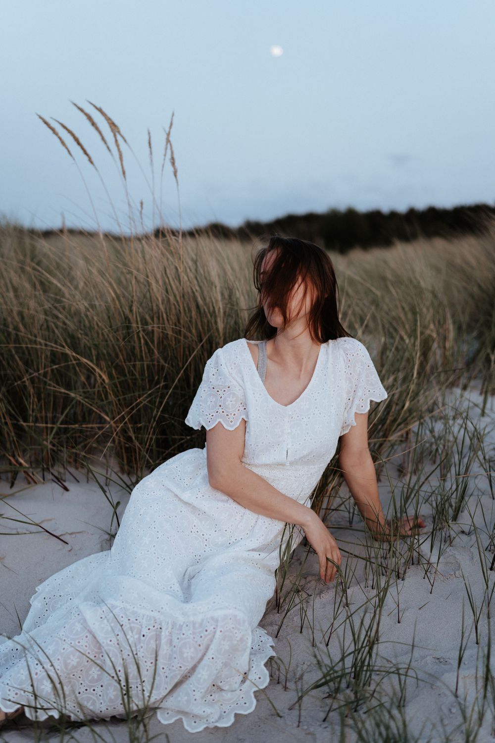 White lace dress creates dreamy coastal scene with beach grass and moon in background.