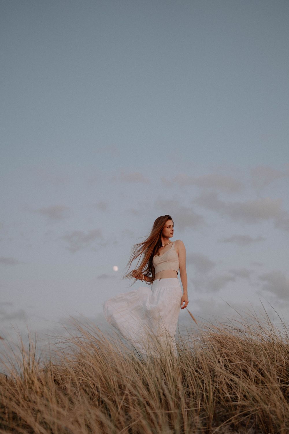 Flowing white skirt catches breeze among coastal dunes at twilight.
