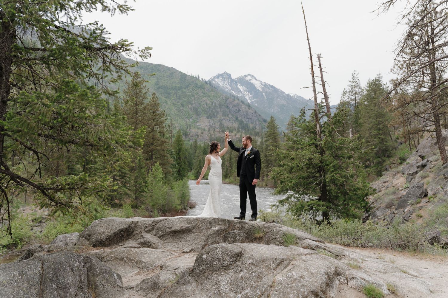 A scenic mountain elopement ceremony takes place along a rocky cliff trail surrounded by evergreen trees and peaks.