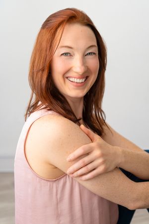Professional portrait of person in pink tank top smiling against white background.